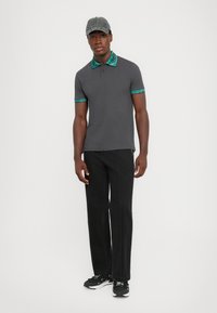 Grå polo skjorte med teal mønstrede krage og erme detaljer, sammen med svarte bukser og svarte sneakers. Generelt uformelt antrekk.