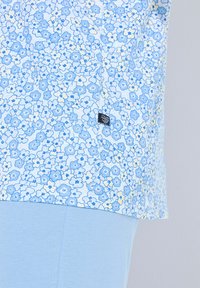 Top corto de manga corta azul claro con un patrón de flores en tonos de azul y amarillo, con una pequeña etiqueta negra en el dobladillo.