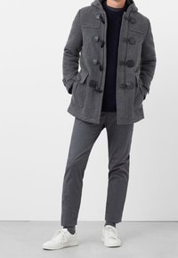 Manteau en mélange de laine gris avec capuche, fermetures à bascule et poches avant, associé à un pantalon gris et des baskets blanches. Design simple et fonctionnel.