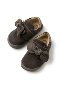 Zapatos de ante marrón oscuro con un gran lazo en la parte delantera, con un forro interior suave y suela texturada. Cierre de tiras de velcro.