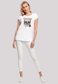 Witte katoenen t-shirt met een zwart schedelafbeelding en een rode roos. Gecombineerd met witte slim-fit broek en witte sneakers.