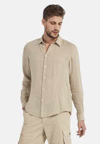 Camicia a maniche lunghe in lino beige con colletto a polo, patta frontale e vestibilità rilassata. Presenta una superficie leggermente texture.