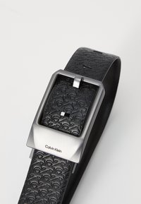 Black leather belt featuring a textured pattern, a silver-tone rectangular buckle, and the "Calvin Klein" logo embossed on the strap.