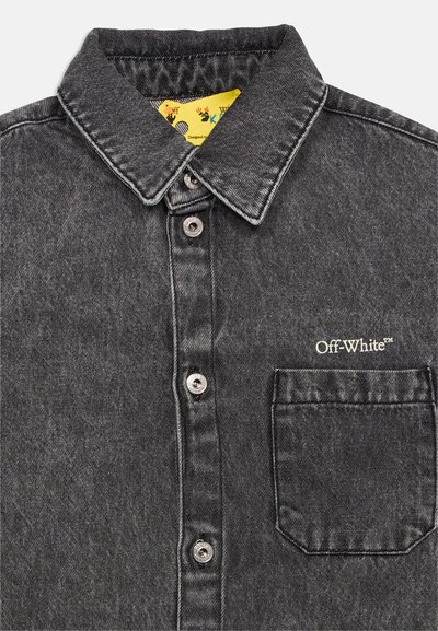 Μαύρο πουκάμισο από τζιν με κουμπιά, μυτερό γιακά, μπροστινή τσέπη και το λογότυπο "Off-White™" κεντημένο πάνω από την τσέπη, με κίτρινη εσωτερική ετικέτα ορατή.