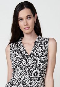 Maglietta senza maniche bianca e nera con un motivo floreale, colletto e bottoni. Presenta due tasche sul petto e una texture di tessuto leggero.