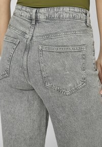 Jeans in denim grigio con vita alta, gambe affusolate e due tasche posteriori. Il tessuto presenta un aspetto texturizzato e sbiadito.