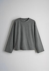 Dark gray long-sleeve crew neck shirt hanging against a plain light gray wall, centered in the frame.
