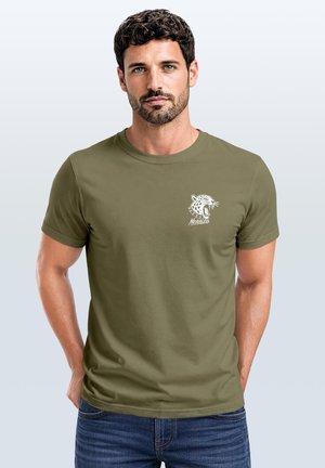 Man with short dark hair and beard wearing olive green t-shirt with white roaring leopard graphic and "Nevertheless" text on chest.