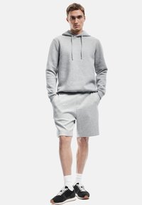 Sudadera con capucha gris y pantalones cortos a juego, hechos de una suave mezcla de algodón. Cuenta con un bolsillo frontal, puños acanalados y zapatos deportivos negros.