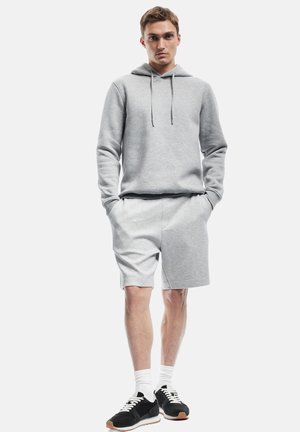 Sweat-shirt à capuche gris et shorts assortis, en mélange de coton doux. Comprend une poche frontale, des poignets côtelés et des chaussures de sport noires.