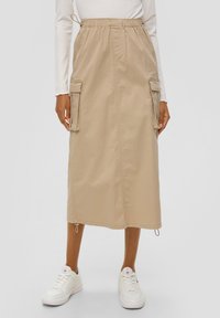 Beige midi-rok met een trekkoord in de taille, zijcargozakken en verstelbare zomen, vervaardigd van lichte stof, gecombineerd met witte sneakers.