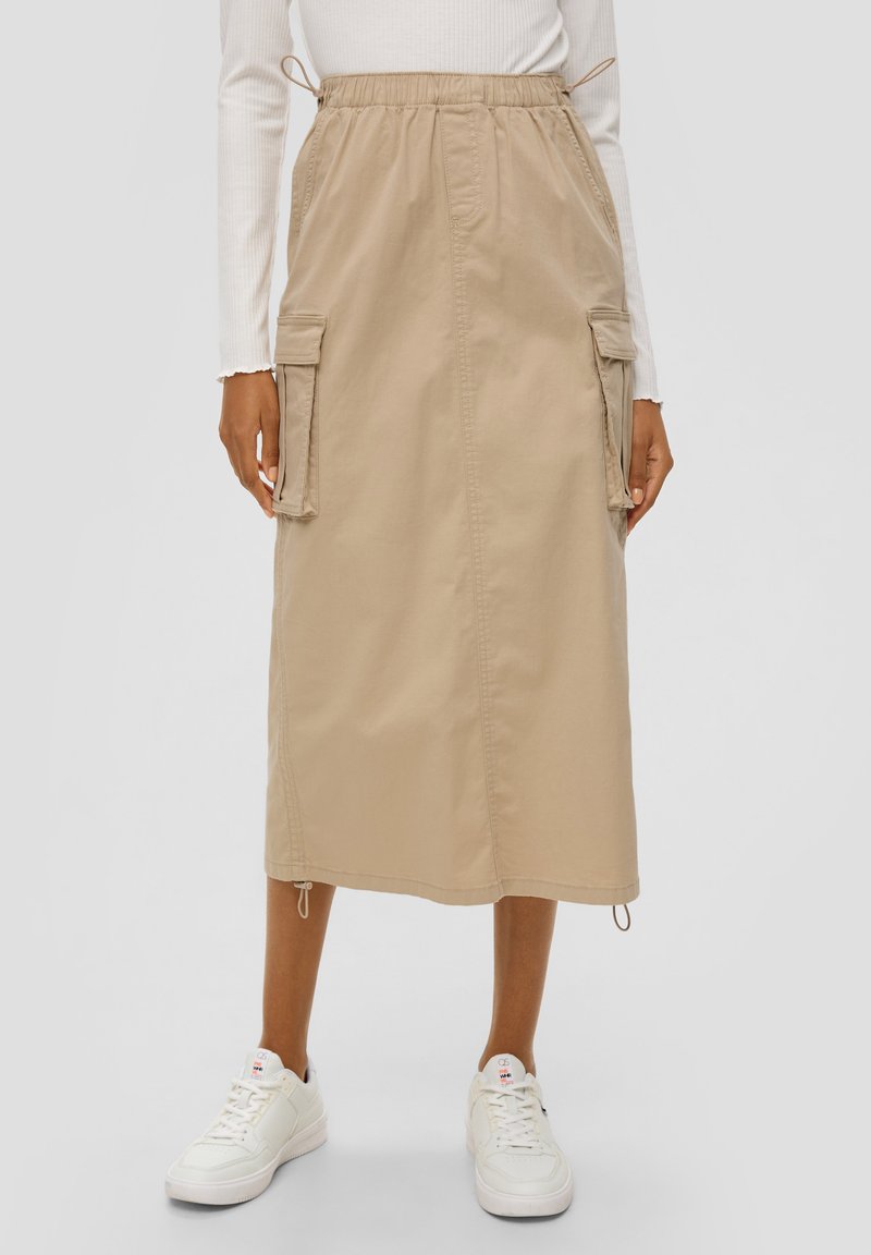 Beige midi-rok met een trekkoord in de taille, zijcargozakken en verstelbare zomen, vervaardigd van lichte stof, gecombineerd met witte sneakers.