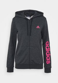 Sweat à capuche gris zippé avec une capuche, arborant un logo Adidas rose sur la poitrine et un texte plus grand "adidas" en rose courant le long de la manche droite.