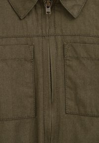 Giacca verde oliva con zip, dotata di due tasche frontali, colletto e cuciture robuste. Il tessuto ha una trama liscia e una finitura resistente.