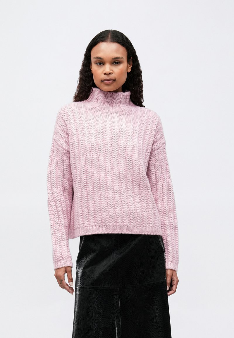 Maglione a coste di un rosa chiaro con collo alto, vestibilità rilassata e maniche lunghe, abbinato a una gonna in similpelle nera. Design semplice e con texture.