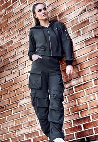 Black cropped hoodie with zip closure and side pockets paired with black cargo pants featuring multiple pockets, textured fabric, and a relaxed fit.