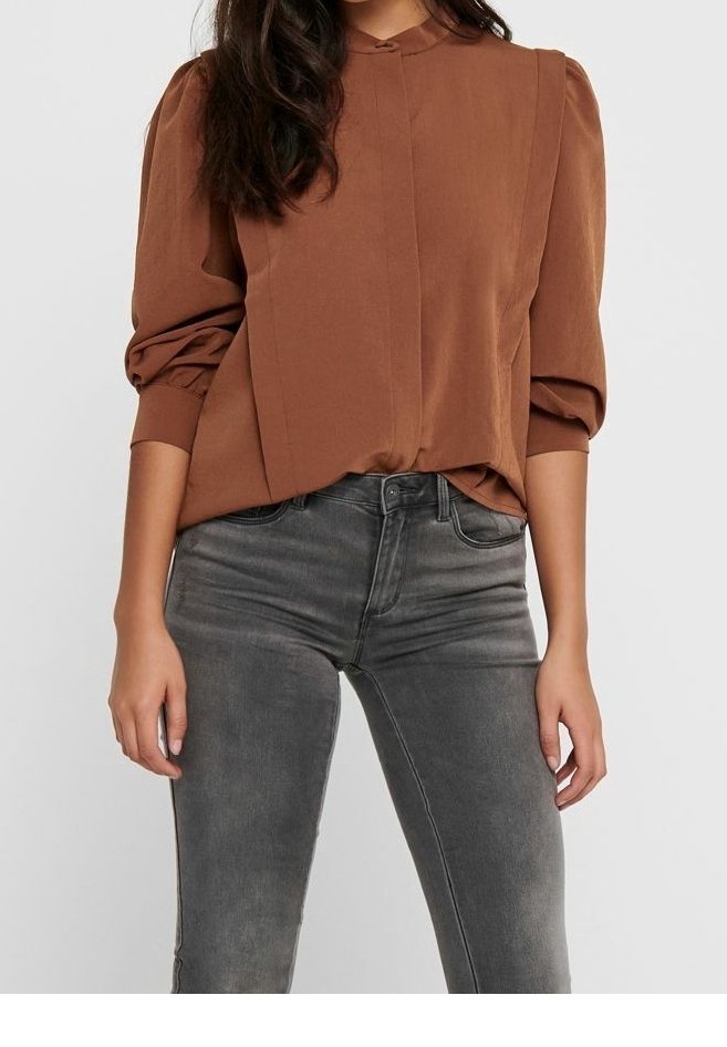 Braune Bluse mit hohem Kragen, puffigen Ärmeln und Vorderfalten, kombiniert mit grauen skinny Jeans in einem verwaschenen Finish.