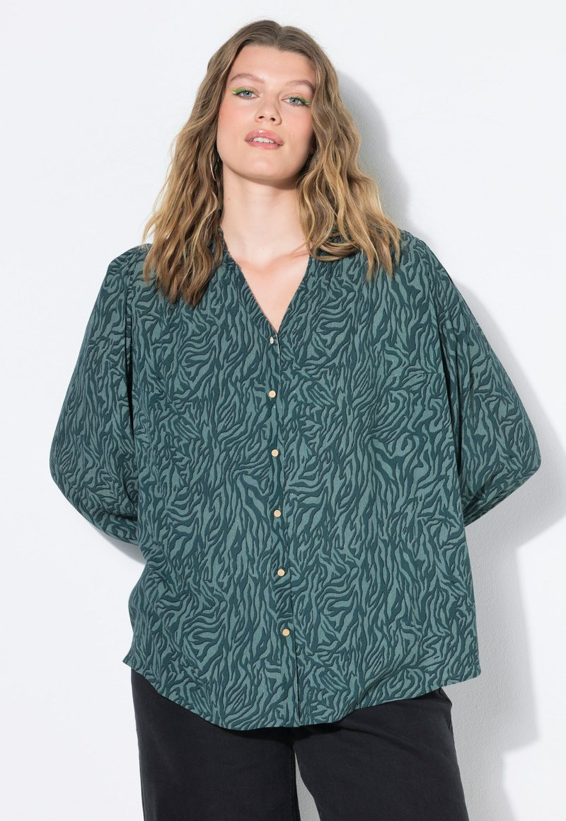 Camicia oversize con bottoni in verde scuro, caratterizzata da una stampa a zebre testurizzata, bottoni dorati e scollo a V. Vestibilità rilassata con maniche ampie.
