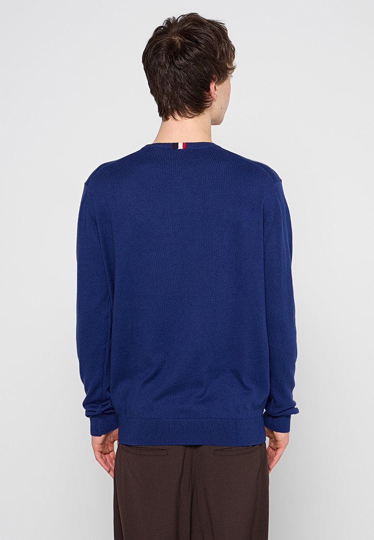 Marineblauer Strickpullover mit geripptem Muster und Rundhalsausschnitt. Verfügt über einen kleinen roten, weißen und blauen Akzent am Ausschnitt.