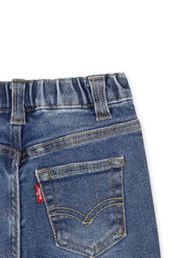 Jeans in denim con cintura elastica, di colore blu scuro. Caratteristiche includono tasca posteriore con etichetta rossa, cuciture arancioni e leggera scoloritura.