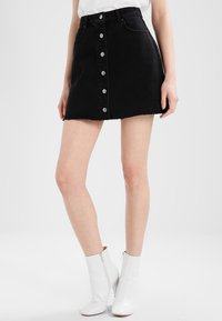 Minifalda de mezclilla negra con cintura alta, cierre de botón en la parte delantera, dobladillo desflecado y diseño clásico de cinco bolsillos.