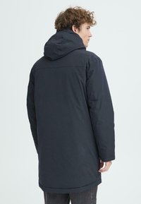 Tumedad sinine isoleeritud parka kapuutsiga, sirge lõike, pikkade varrukate ja küljetaskutega. Sile tekstuur ja minimalistlik disain.