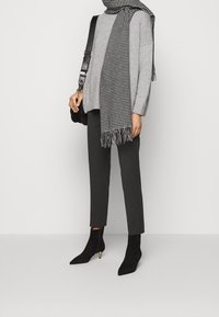 Grå striktrøje, sort-hvidt hundetandsternet tørklæde med frynser, mørkegrå bukser og sorte ankelstøvler med spidst tådesign og guld-accenter.