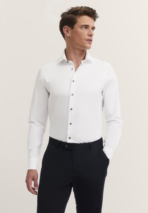 White long-sleeve shirt with a slim fit, featuring black buttons and a fold-down collar, paired with black trousers. Smooth fabric texture.
