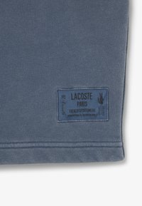 Tessuto in cotone blu per felpa, con etichetta cucita contenente il nome del marchio, dettagli stilistici e un piccolo logo. Texture liscia, design casual.