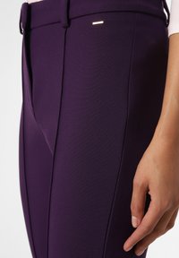 Lila högmidjade byxor i texturerat tyg, med en subtil guldaccents samt sidofållar för en skräddarsydd passform.