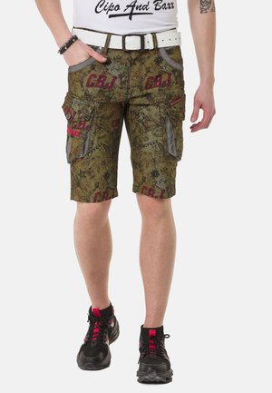 Shorts cargo en vert olive avec un motif détaillé, comprenant des poches latérales, des accents gris contrastants et un texte de logo rouge. Portés avec des baskets noires.