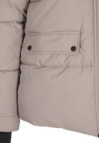 Giacca puffer beige chiaro con texture trapuntata, dotata di una tasca con patta fissata da un bottone a pressione nero sul lato sinistro.