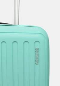 Valigia rigida di colore verde menta, con strisce testurizzate, manico telescopico in argento e logo del marchio in rilievo sul lato.