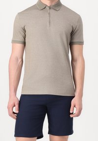 Polo à manches courtes en tissu kaki avec un col zippé et des accents de couleur vert foncé contrastants au col et aux manches, associé à un short foncé.