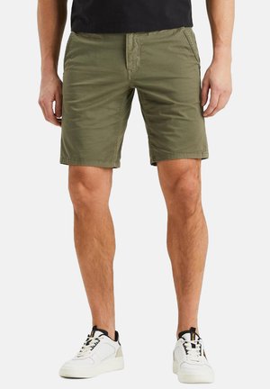 Pantalones cortos de algodón verde oliva, hasta la rodilla, con bolsillos delanteros y cremallera. Llevados con zapatillas blancas, con detalles en negro.