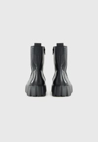 Botas de tobillo de cuero negro con suela de goma gruesa, que presentan una textura suave y cremalleras laterales para facilitar su uso.