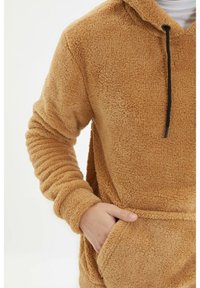 Miękka, jasnobrązowa bluza z kapturem, posiadająca przednią kieszeń, sznurek do regulacji kaptura oraz ściągacze na rękawach. Miękka w dotyku o luźnym kroju, idealna dla wygody.