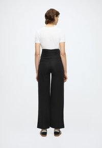 Μαύρο παντελόνι με φαρδιά παντελόνα και ψηλή, σούρα μέση, συνδυασμένο με εφαρμοστή λευκή μπλούζα και μαύρα αθλητικά παπούτσια με λευκές λεπτομέρειες.