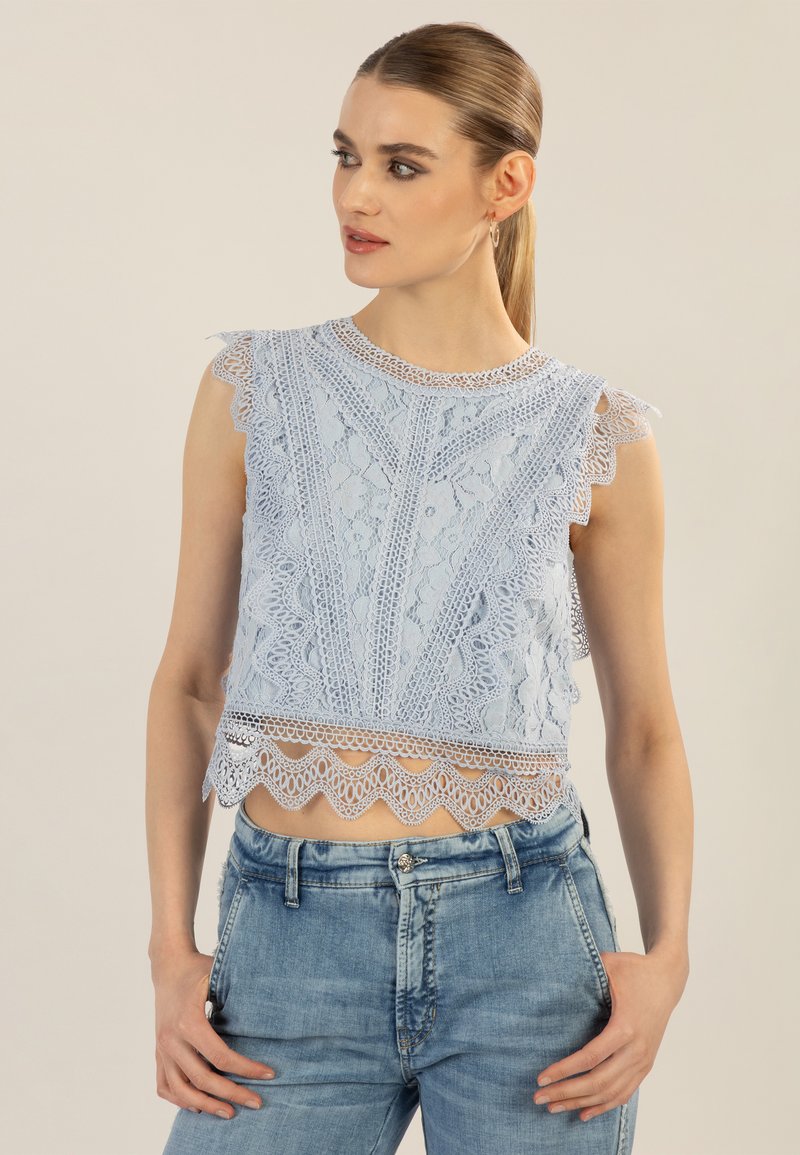 Helles blauer Spitze-Crop-Top mit gewellten Kanten, filigranen Mustern und kurzen Ärmeln, kombiniert mit hellblauen Jeans.