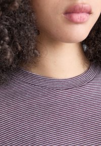 Lilla stripete t-skjorte med ribbet halslinning, med fine vertikale striper i varierende nyanser og en myk, teksturert stoffoverflate.