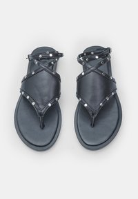 Zwarte leren sandalen met gekruiste banden, zilveren studs, rubberen zool en teenslipper-ontwerp. Soepele textuur en minimalistische esthetiek.