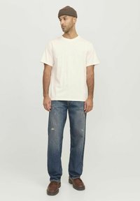 Light beige cotton t-shirt, relaxed fit, short sleeves. Worn with distressed blue denim jeans and brown leather shoes. Brown knit beanie.