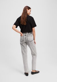 Jeans in denim grigio a vita alta con una finitura sbiadita, abbinati a una t-shirt nera a maniche corte e scarpe nere a pois.