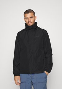Veste noire imperméable avec un col haut et une capuche réglable. Équipée de poignets élastiques et d'un logo discret sur la poitrine. Texture lisse.