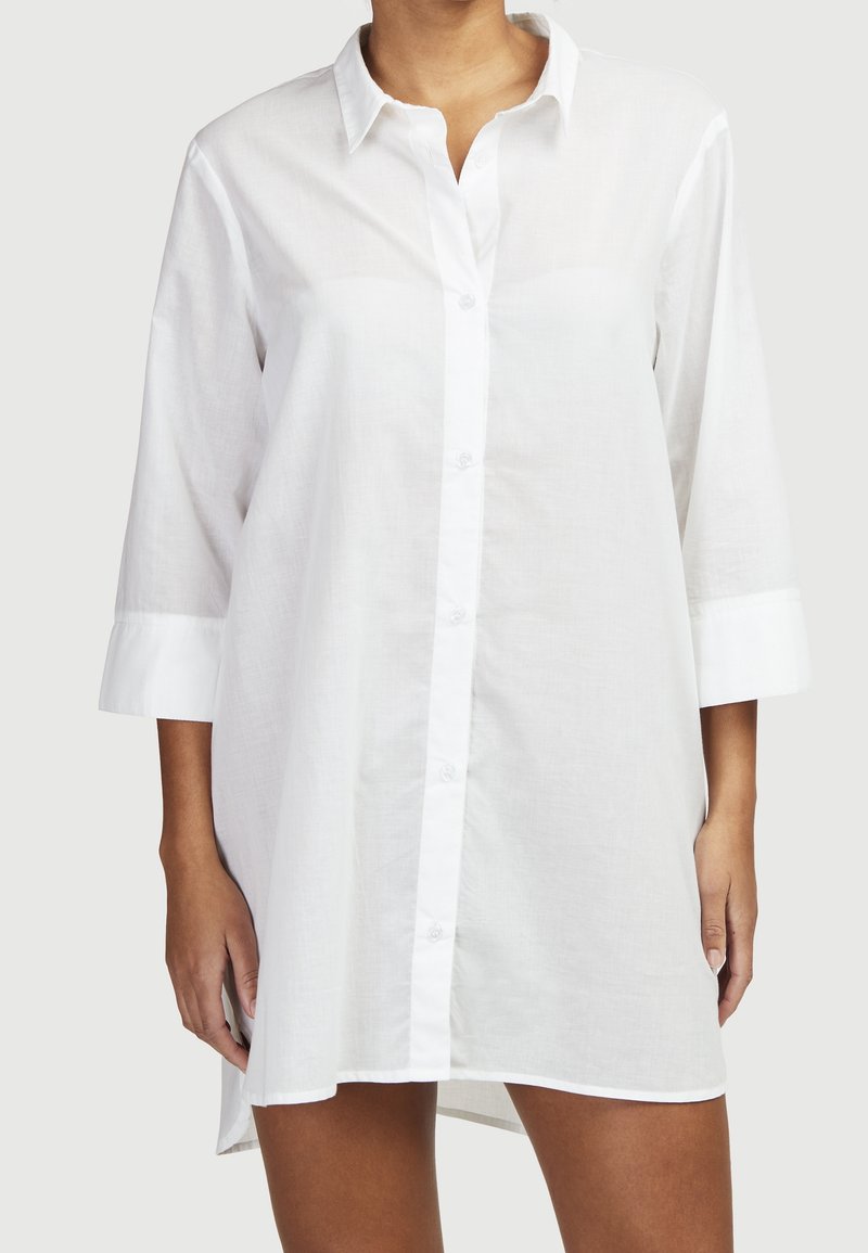 Weißes Hemd zum Knöpfen mit lockerem Schnitt, langen Ärmeln und einem leicht längeren Rückensaum. Hergestellt aus leichtem, atmungsaktivem Stoff.