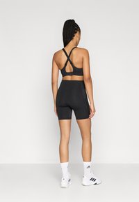 Czarny sportowy biustonosz z haftką na plecach, zestawiony z czarnymi, wysokim stanem szortami. Strój charakteryzuje się gładką teksturą i minimalistycznym stylem.