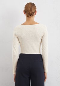 Hellbeige Langarmoberteil mit weitem Ausschnitt, kombiniert mit dunkelblauen, hoch taillierten Hosen mit einer Gesäßtasche. Glatte Textur, lässige Passform.