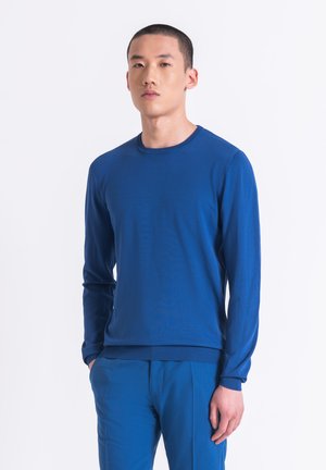 Camicia blu a maniche lunghe in un tessuto morbido con colletto tondo e finiture a costine, abbinata a pantaloni blu coordinati. Colore solido, design minimale.