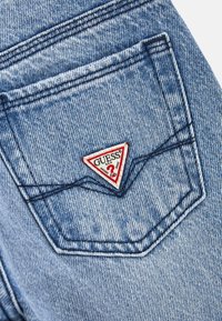 Jeans in denim di colore azzurro chiaro, con una patch triangolare rossa e bianca distintiva sulla tasca posteriore. Texture slavata e dettagli di cucitura.