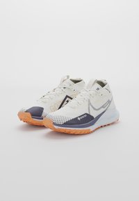 Baskets de course Nike Gore-Tex blanches et orange à tige haute et semelles texturées, placées côte à côte sur un fond blanc.